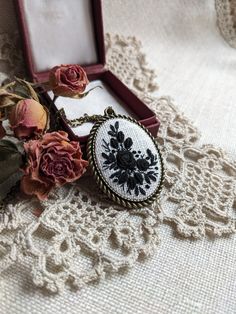 an embroidered necklace with flowers in it sitting on a lace tablecloth next to a box