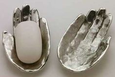 two metal dishes with an egg in one and a hand on the other, both