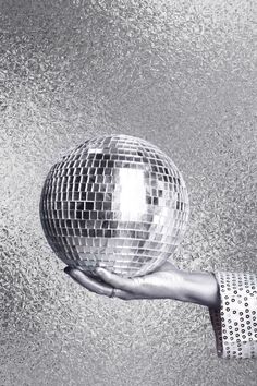 a person's hand holding a disco ball in front of a mirror surface background