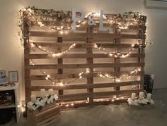 a wooden pallet with candles and flowers on it is decorated with fairy lights, greenery and the word p & l