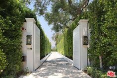 an open driveway with two white doors leading into the distance is surrounded by trees and bushes