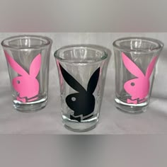 three shot glasses with pink and black bunny ears on the side, one is empty