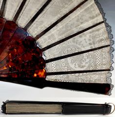 an old fan with lace on it sitting next to a book