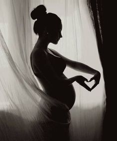 a pregnant woman standing in front of a curtain with her hand on her belly and the other arm behind her back