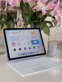 a laptop computer sitting on top of a desk next to flowers and a glass vase