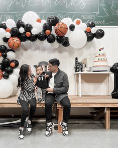 a man and woman sitting on a bench next to a child in front of balloons