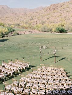 an outdoor ceremony setup with chairs and flowers in the grass, surrounded by mountains on either side