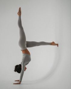 a woman doing a handstand on one leg in front of a white background