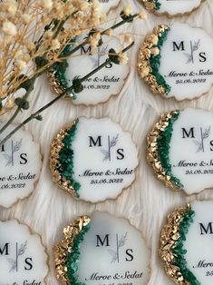 wedding cookies decorated with gold and green frosting are arranged on a white tablecloth