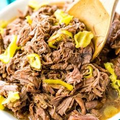 a white bowl filled with meat and vegetables on top of a table next to a wooden spoon