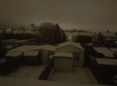 an aerial view of snow covered rooftops and houses in the distance at night time