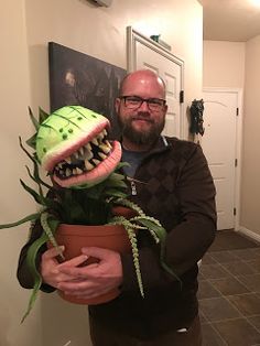 a man holding a potted plant with a fake monster's mouth on it