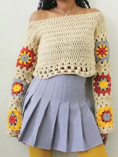 a woman wearing a crochet sweater with flowers on the sleeves, and a pleated skirt