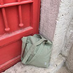 a green and white checkered bag sitting next to a red door on the side of a building