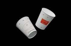 two white coffee cups sitting next to each other on a black surface with red lines