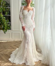 a woman in a white wedding dress standing on a wooden floor next to a window