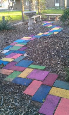 a walkway made out of colored blocks in the yard with a bench and tree behind it