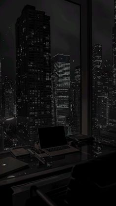 a laptop computer sitting on top of a desk in front of a window overlooking a city at night