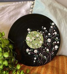 a record with flowers painted on it sitting next to a potted plant and pillow