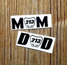 two stickers with the words mom and dad in black on wooden background, closeup