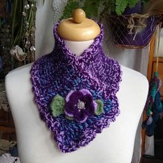 a purple and green crocheted scarf on a mannequin headpiece with a flower