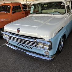 an old blue and white pickup truck parked in a parking lot next to other trucks