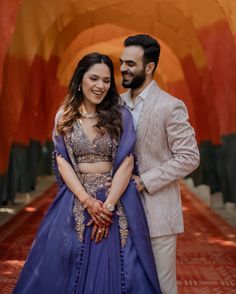 a man and woman standing next to each other in front of an orange wall wearing blue outfits