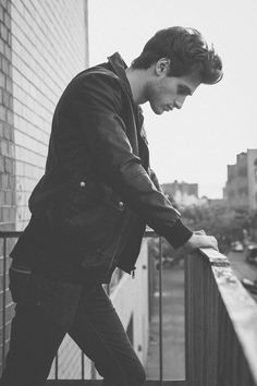 black and white photograph of a young man leaning on a railing looking down at his cell phone