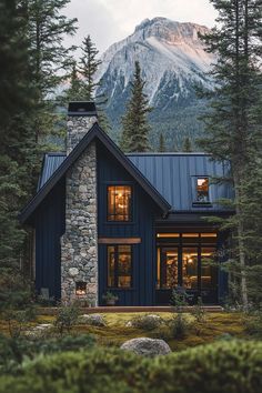 a house in the woods with mountains in the background and lights on at the windows