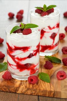 two desserts with raspberries and whipped cream in them on a wooden board