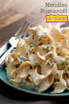 a blue plate topped with pasta covered in cheese and herbs next to a fork on a wooden table