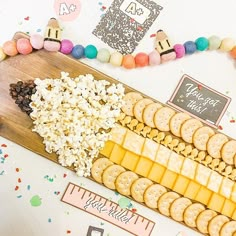 a wooden cutting board topped with cheese, crackers and other snacks on top of a table