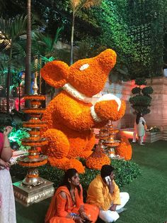 people sitting on the ground in front of a large teddy bear made out of flowers