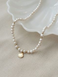 This genuine baroque Pearl necklace is the perfect accessory to elevate your summer look! This stunning necklace is crafted with off round irregular pearls and features a beautiful 14K Gold Filled or 925 Silver scallop shell charm. It's the perfect addition to your jewelry collection and is sure to become a beachy ocean inspired wardrobe staple.  * 14K Gold Filled or 925 Sterling Silver accents * Adjustable 18" - 20" length * 10mm 14K Gold Filled or 925 Sterling Silver Scallop Shell charm * Natu Beaded Necklace With Baroque Pearl And Pearl Charm, Beaded Necklace With Baroque Pearl Charm, Shell-shaped Pearl Charm Necklaces, Beaded Shell Pearl Necklace, Pearl Beaded Necklace In Shell Shape, Shell-shaped Pearl Drop Necklace, Beaded Pearl Necklace With Shell Shape, Shell-shaped Pearl Necklace With Pearl Pendant, Pearl Drop Shell Pearl Necklace