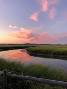 the sun is setting over a marshy area with water and grass in the foreground