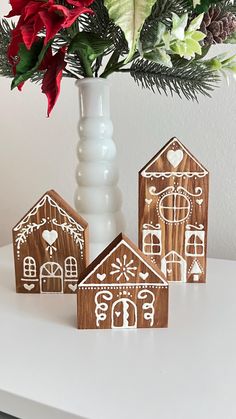 three wooden gingerbread houses are sitting on a table next to a vase with flowers