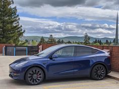 a blue car parked in front of a brick wall with mountains in the back ground