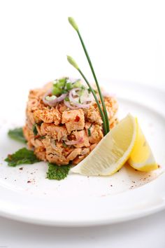 a white plate topped with food next to a lemon wedge and green garnish