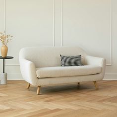 a white couch sitting on top of a hard wood floor next to a vase filled with flowers