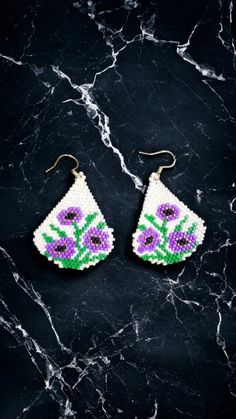 two pairs of beaded earrings with flowers on them sitting on top of a marble surface