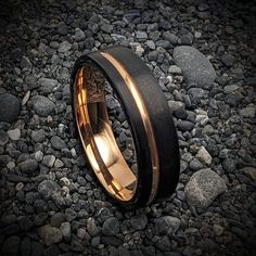 two wedding bands with gold and black inlays are on the ground next to some rocks