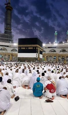 many people are sitting on the ground in front of an open air mosque at night