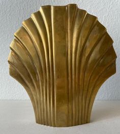 a gold shell shaped vase sitting on top of a white tablecloth covered floor next to a wall