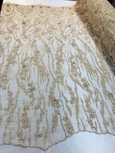 a white table cloth with gold sequins and beads on it, sitting on top of a bed