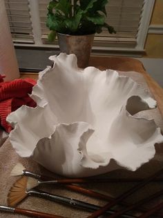 a white bowl sitting on top of a table next to paint brushes and a potted plant