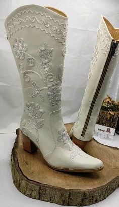 a pair of white cowboy boots sitting on top of a wooden stump