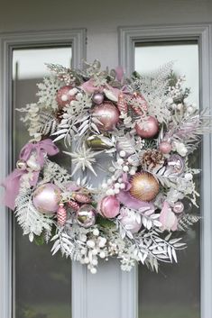 a wreath is hanging on the front door with pink and silver ornaments around it's edges