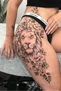 a woman's thigh with a lion tattoo and flowers on the side, sitting on a table