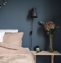 a vase with flowers sitting on a table next to a night stand and lamp in a bedroom