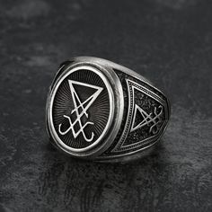 a silver ring with an inverted symbol on the front and sides, sitting on a black surface